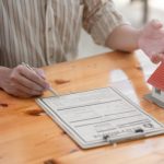 Person reviewing an insurance claim form on a wooden table, with a small house model, illustrating claims assistance services by Santex Public Adjusters.