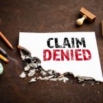 Claim denied document with torn edges, emphasizing insurance claim challenges, surrounded by office supplies, symbolizing assistance with denied home insurance claims.