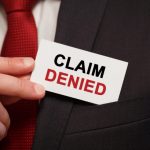 Person in a suit holding a sign that reads "CLAIM DENIED," illustrating the challenges of denied insurance claims.