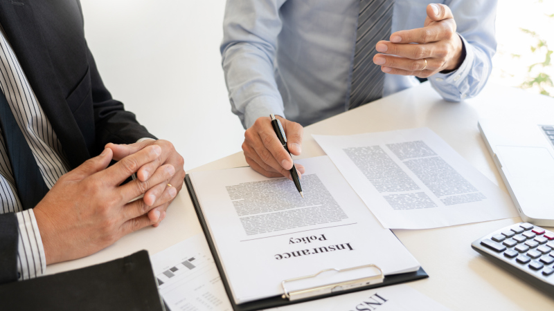 Two professionals discussing an insurance policy, with one pointing at the document while the other listens, emphasizing the role of public insurance adjusters in claims assistance.
